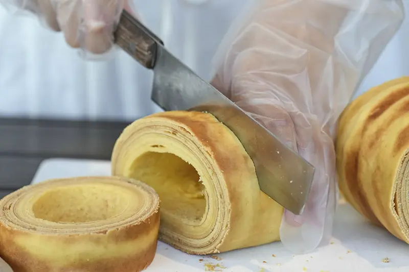 Staff and participants cut Baumkuchen, a German layered cake, during a workshop of Juchheim Ninoshima Welcome Center and Outdoor Activity Camp Monday, July 7, 2025, at Ninoshima island in Hiroshima, western Japan. (AP Photo/Eugene Hoshiko)