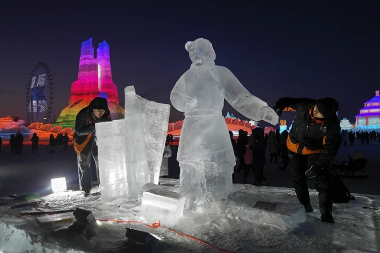 Artists work on a ice sculptures as visitors tour the illuminated ice structures at the Harbin Ice and Snow World in Harbin, China’s Heilongjiang province on Sunday, Jan. 5, 2025. (AP Photo/Andy Wong)