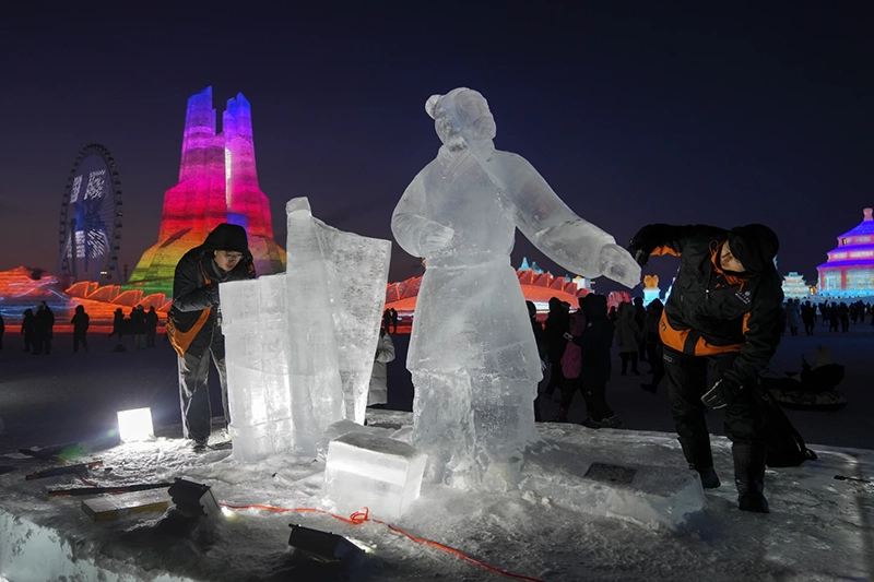 Artists work on a ice sculptures as visitors tour the illuminated ice structures at the Harbin Ice and Snow World in Harbin, China’s Heilongjiang province on Sunday, Jan. 5, 2025. (AP Photo/Andy Wong)