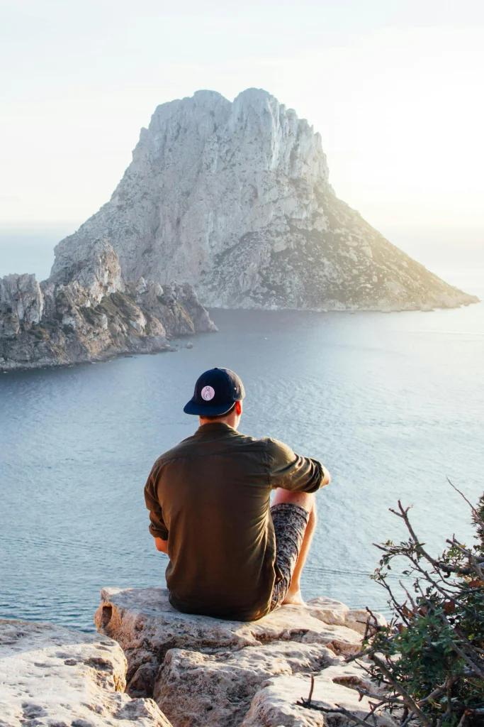 Rear View of Man Sitting on Rock by Sea. Photo by Riccardo.